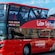 A double decker bus with an open top in front of the Cristo Rei monument in Lisbon